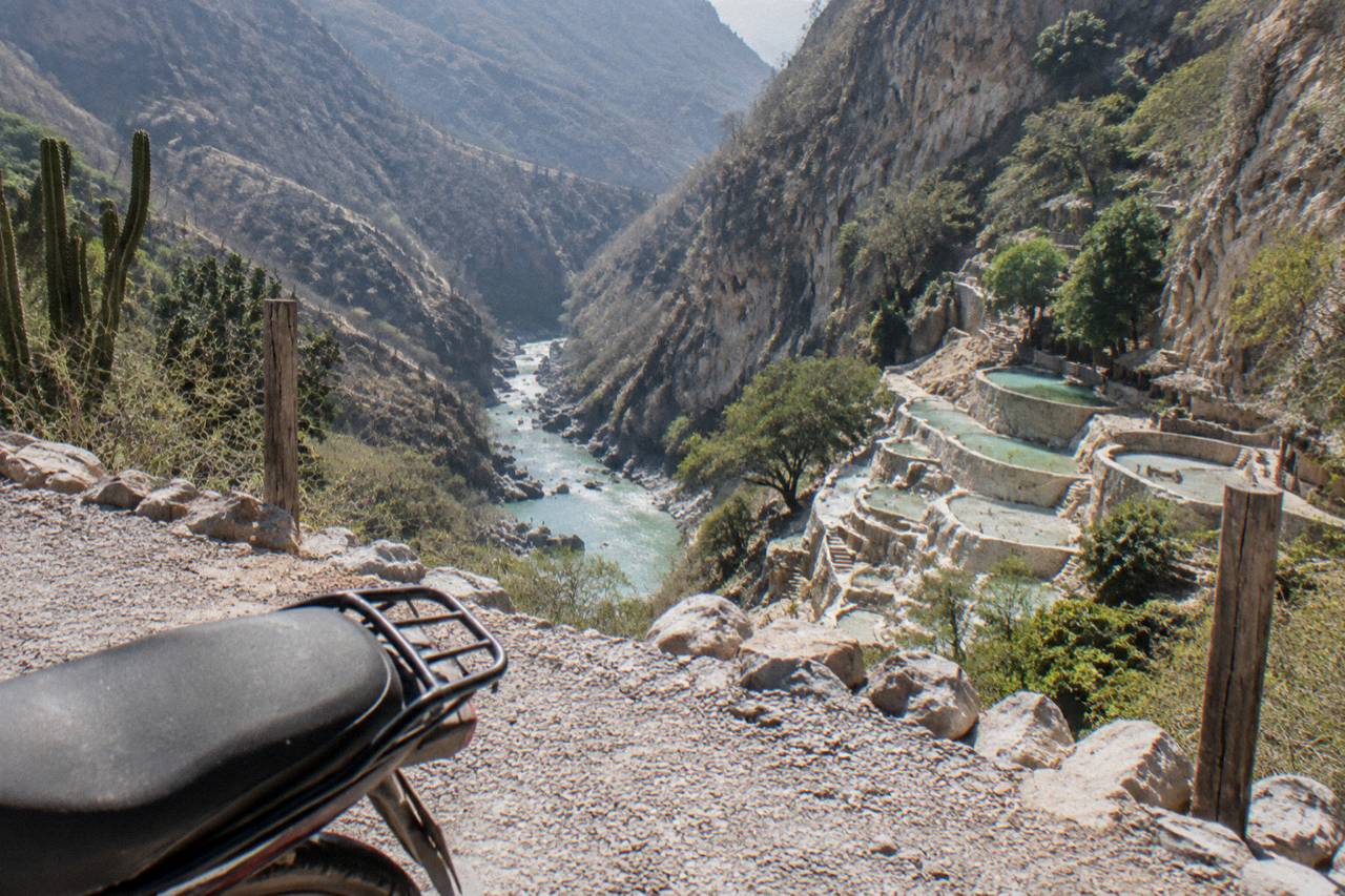 A viewpoint path above a canyon with a river winding below and pools cut into the far cliff