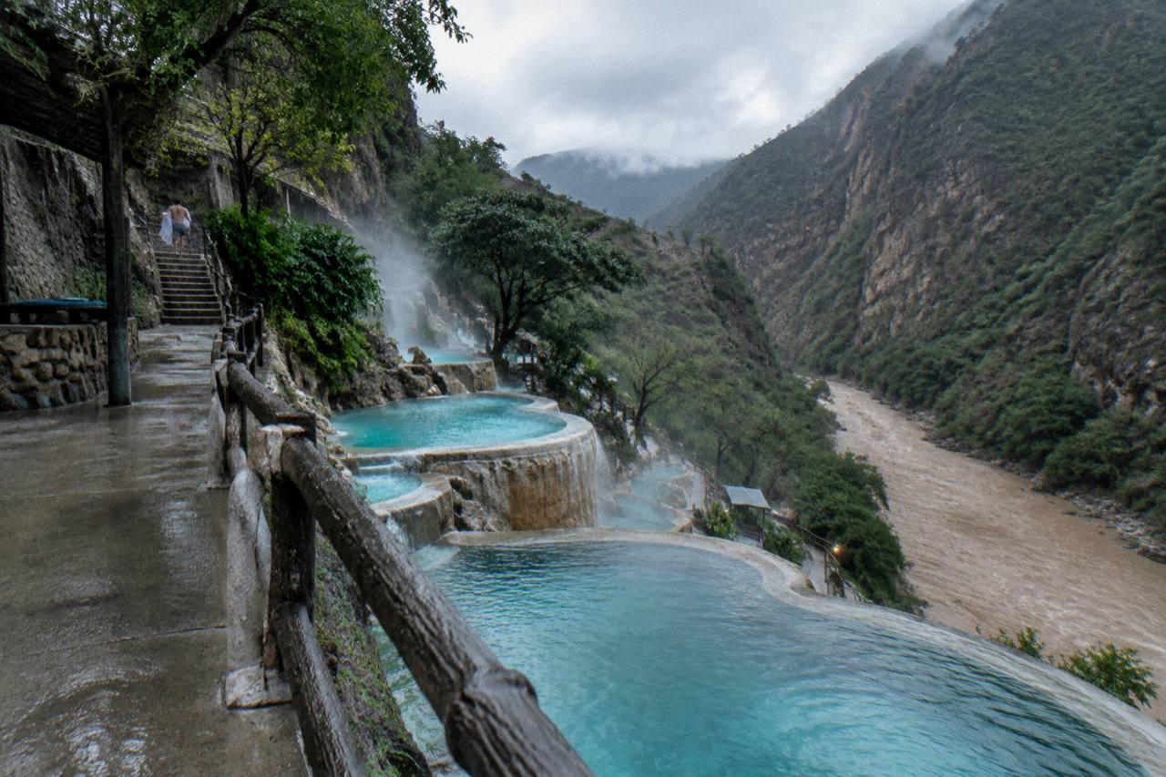 Steaming turquoise pools on a canyon wall seen from an elevated walkway in soft light