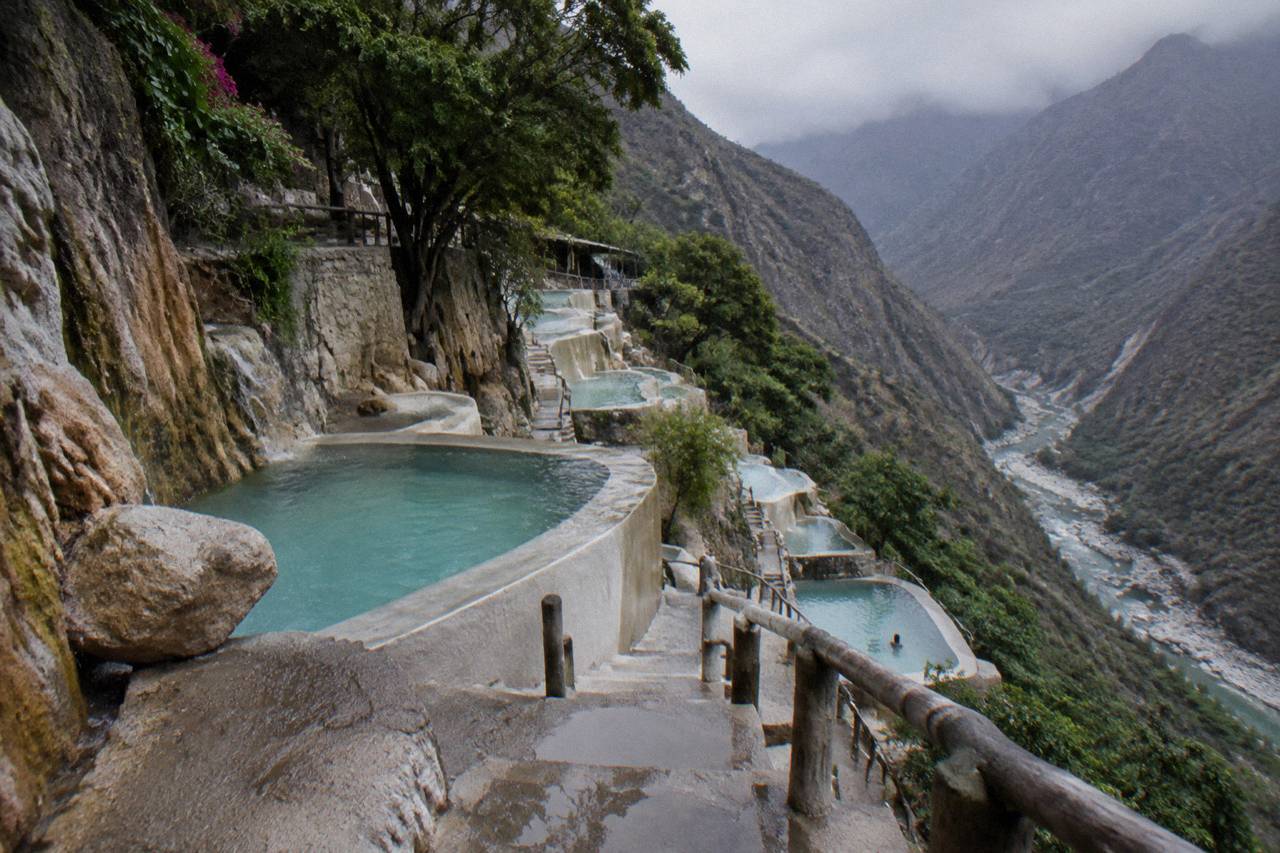 Rows of stone thermal pools along a canyon wall with mountains in the background
