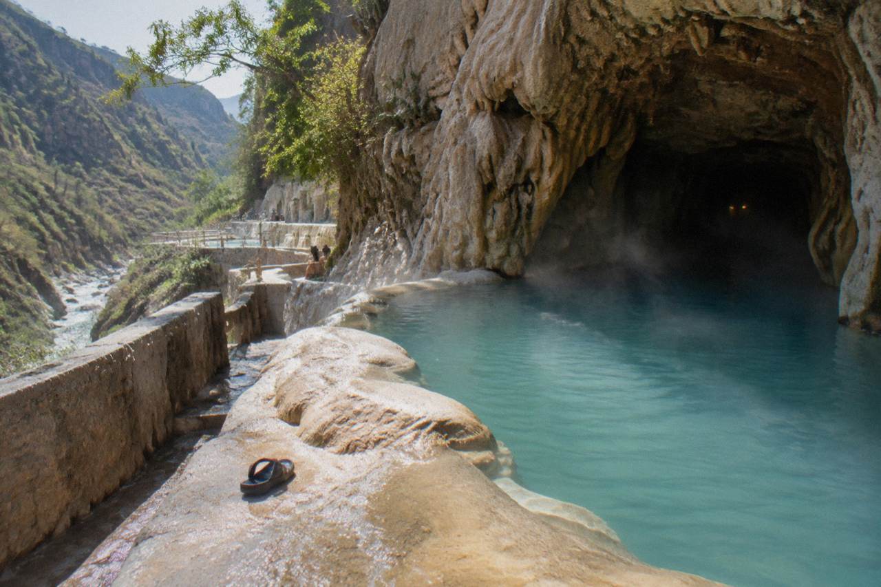 Steam rising from a warm thermal pool at the base of a narrow canyon at midday