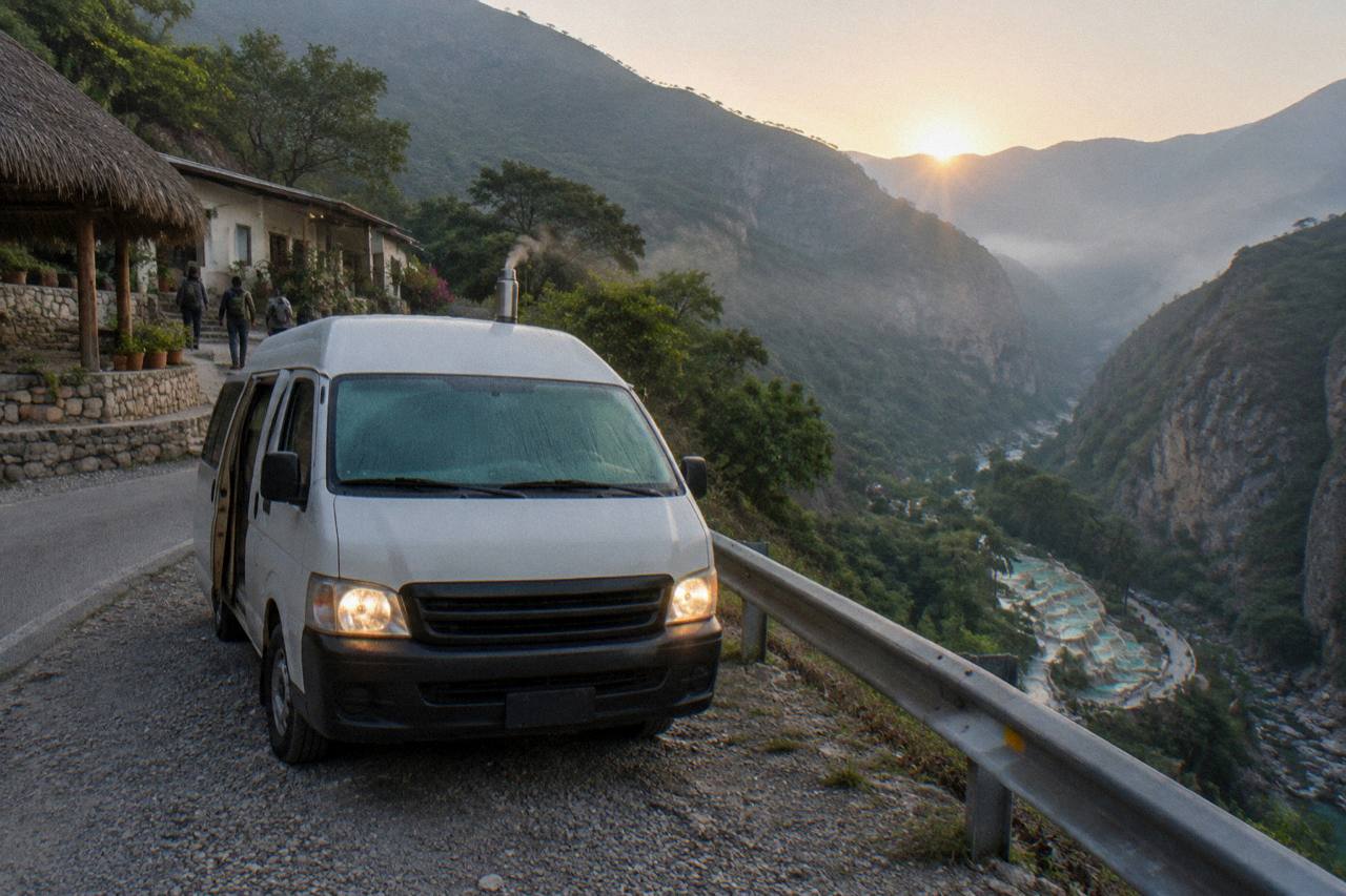 Tour van parked on a mountain road above a green canyon at sunrise