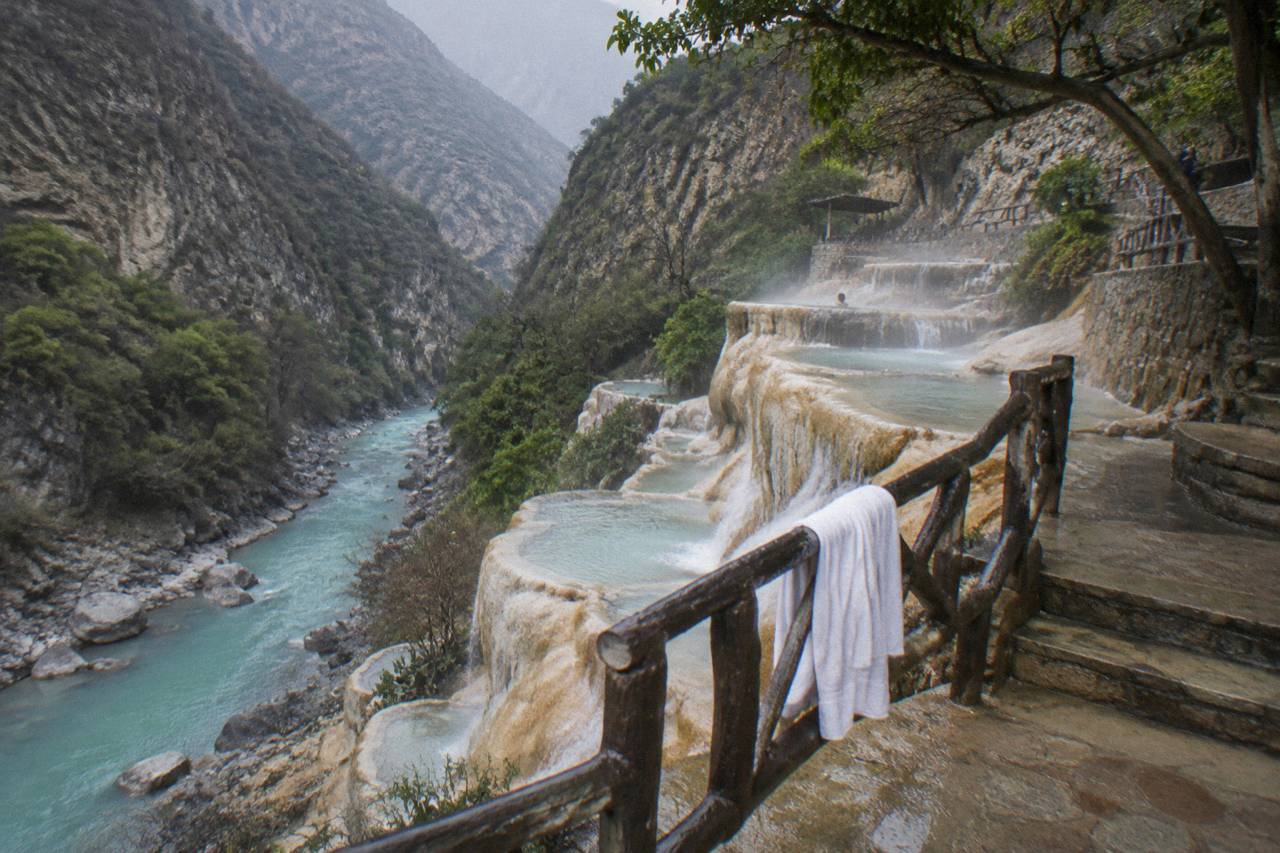 Warm waterfalls spilling down a rock face beside cliffside pools at Tolantongo