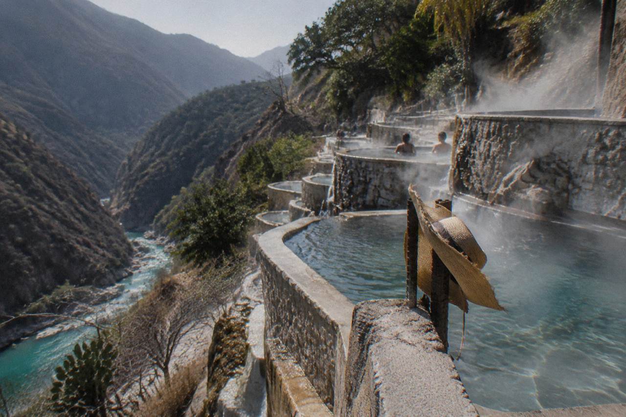 Rows of small terraced thermal pools built into a green canyon cliffside