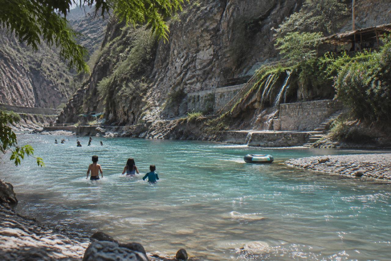 Visitors wading in a shallow warm turquoise river beneath tall canyon cliffs