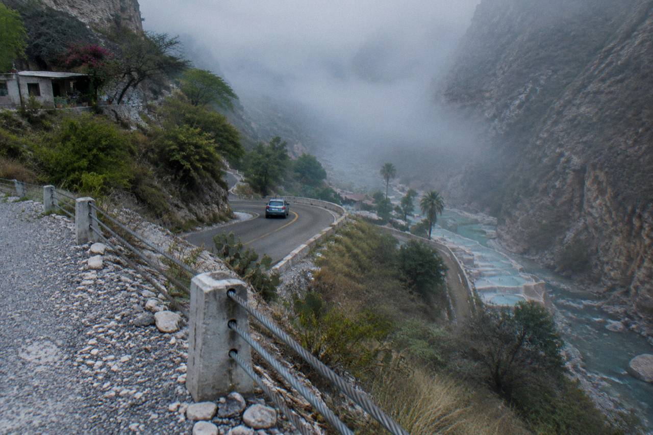 Winding mountain road descending into the Tolantongo canyon with a car rounding a tight corner