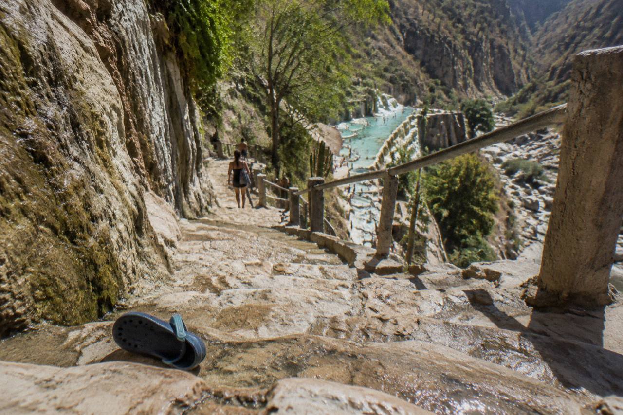 Stepped stone walkways leading down a canyon wall toward warm pools