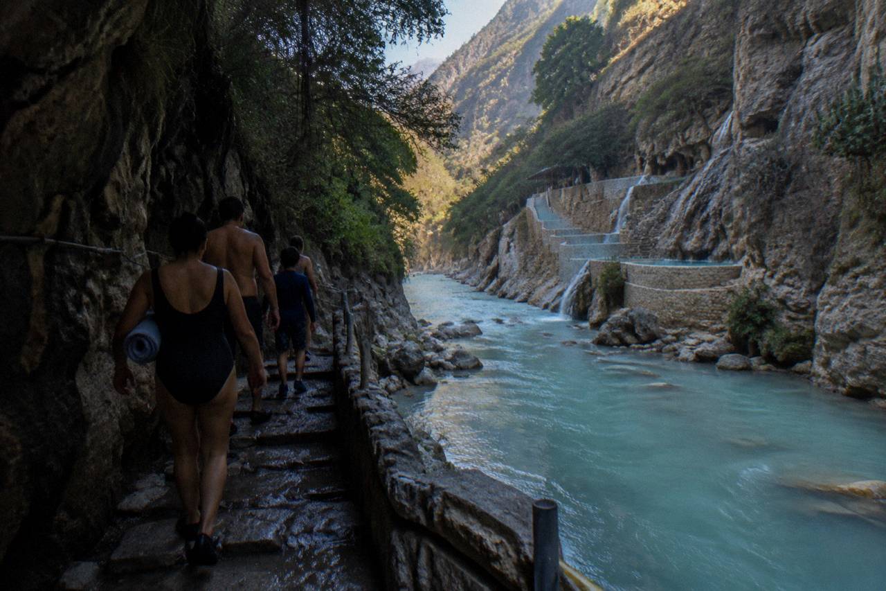 Family walking a narrow canyon path beside the thermal river