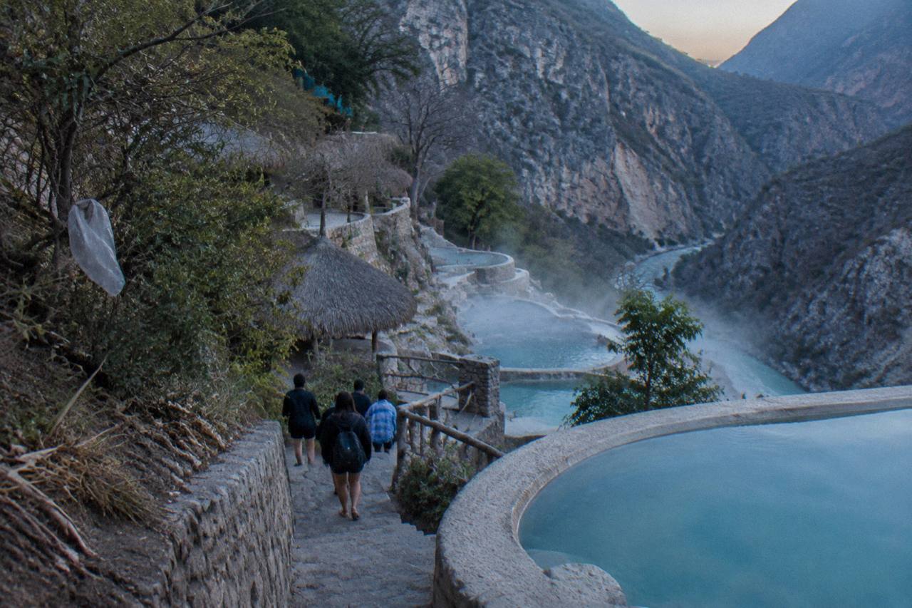 Tour group walking a stone path toward cliffside thermal pools in the canyon