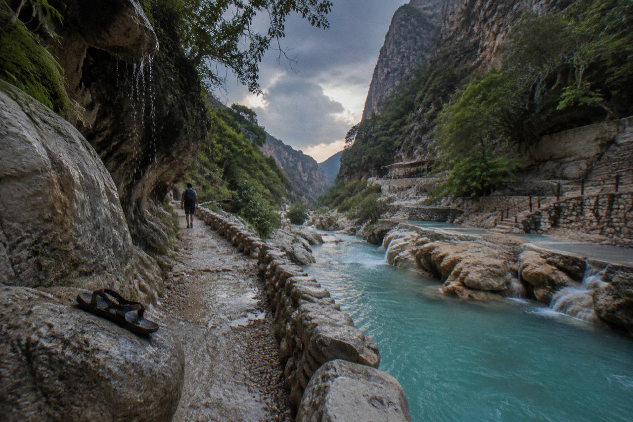 Rocky trail beside the turquoise thermal river with canyon walls rising above