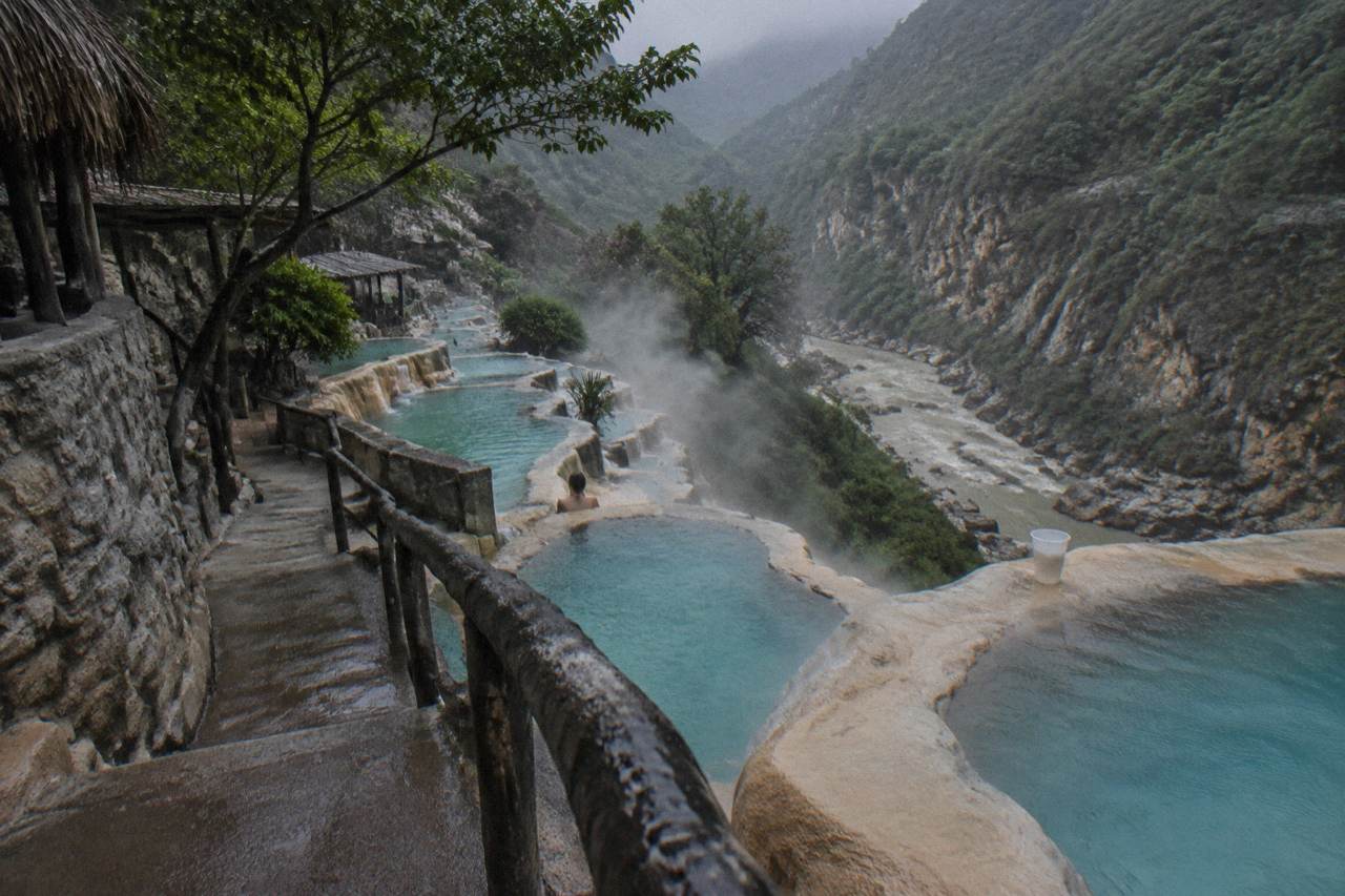 Steep cliffside lined with small turquoise thermal pools overlooking the canyon
