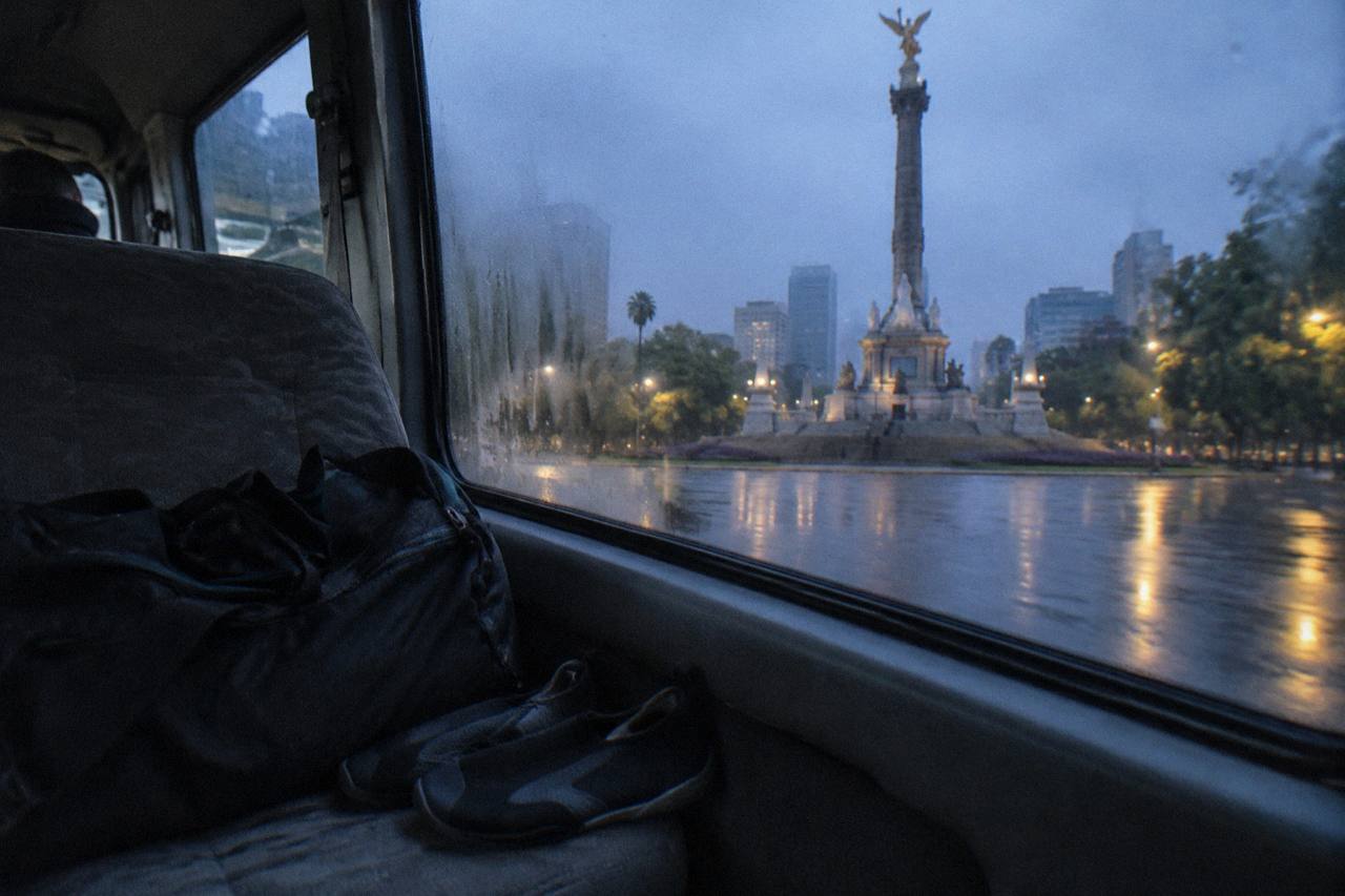 Duffel bag and water shoes on a bus seat before dawn beside a cooler morning road