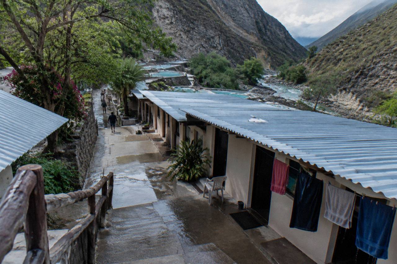 Row of simple lodging rooms with a covered terrace above thermal pools