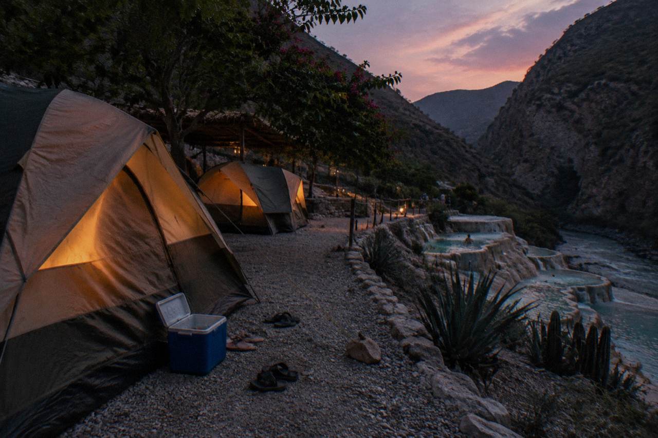 Campground tents pitched on a terrace beside the thermal river at dusk