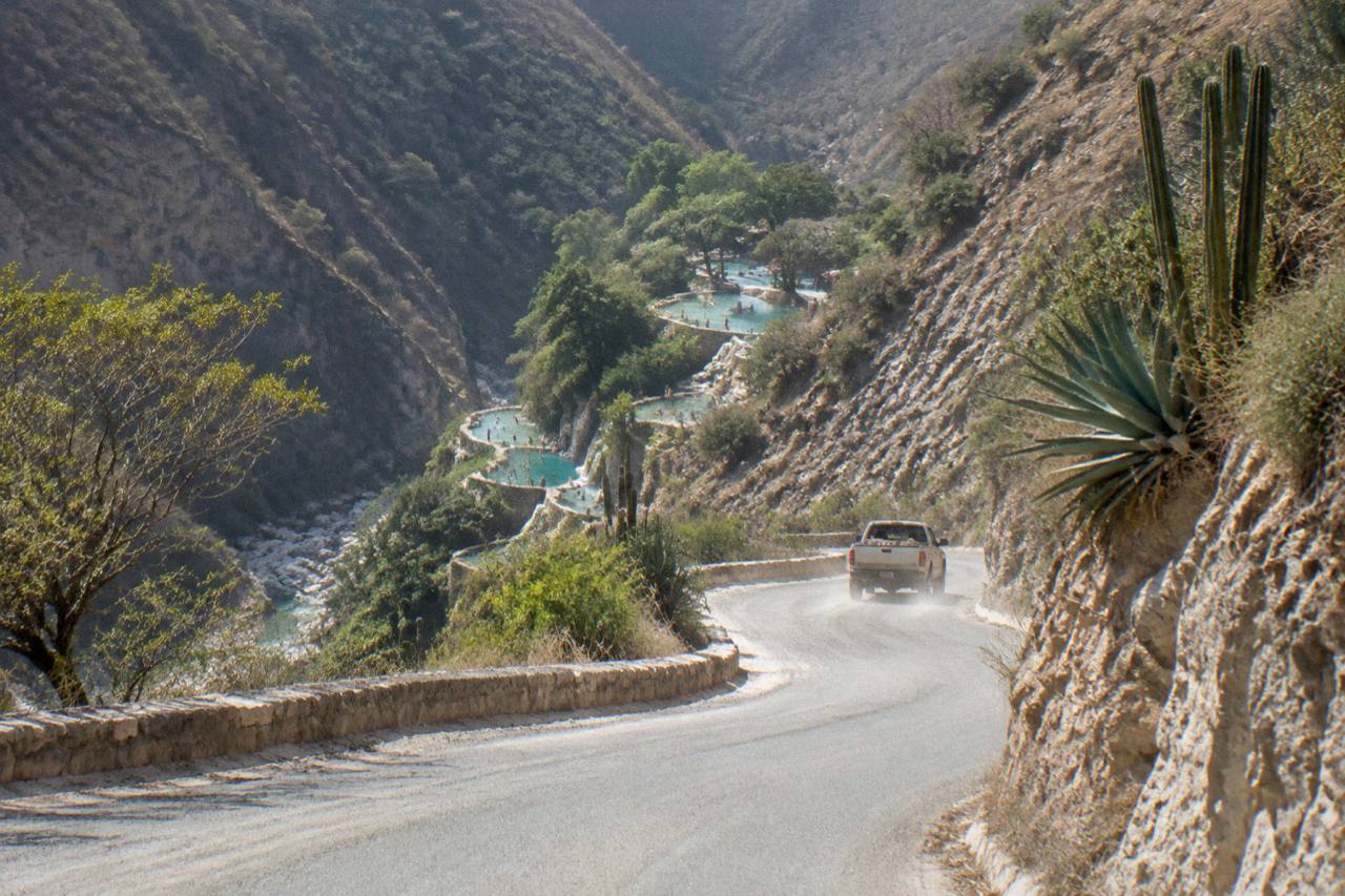 Mountain road switchbacks descending toward the canyon with the park visible below